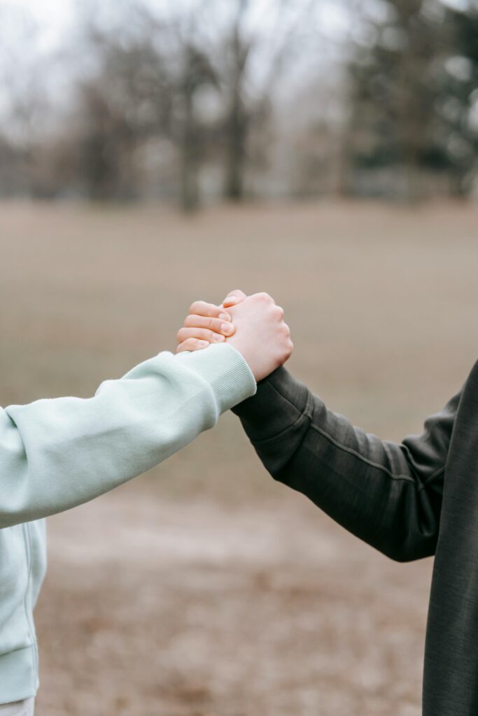 pexels-photo-6551313-6551313 Two adults holding hands in an outdoor park setting, symbolizing trust and connection.